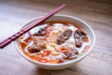 Beef noodle ramen meal with tomato sauce broth in bowl on bright wooden table, famous chinese style food in Taiwan, close up, top view, copy spaceの写真素材