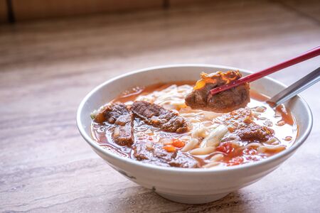 Beef noodle ramen meal with tomato sauce broth in bowl on bright wooden table, famous chinese style...