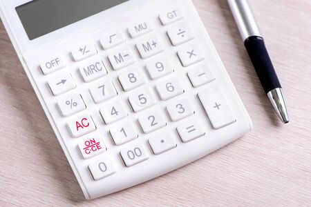 White calculator and pen on bright wooden table, analytics and statistics of financial profit, investment risk concept, copy space, macro, close upの写真素材