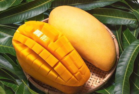 diced mango fruit in bamboo basket on green leaves background, top view, close up, macro, copy space. Tropical summer concept.