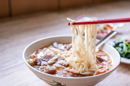 Beef noodle - Taiwan ramen meal with tomato sauce broth in bowl on bright wooden table, famous chinese style food, close up, top view, copy spaceの写真素材