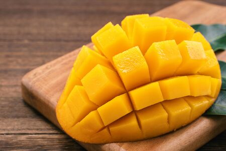 Fresh Mango - Juicy chopped mango cubes on wooden cutting board and rustic timber background. Tropical summer concept. Close up, macro, copy space.の写真素材