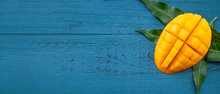 Fresh mango - Juicy chopped fruit with green leaves on dark blue timber background. Tropical fruit design concept. Flat lay. Top view. Copy spaceの写真素材