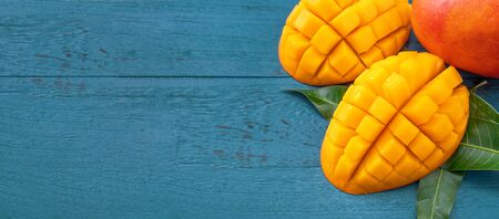 Fresh mango - Juicy chopped fruit with green leaves on dark blue timber background. Tropical fruit design concept. Flat lay. Top view. Copy spaceの写真素材