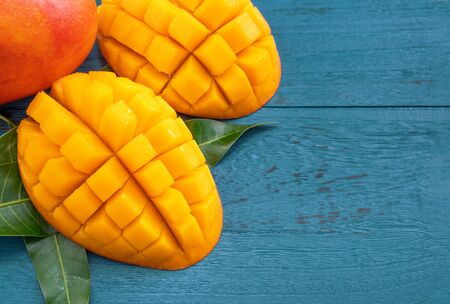 Fresh mango - Juicy chopped fruit with green leaves on dark blue timber background. Tropical fruit design concept. Flat lay. Top view. Copy spaceの写真素材