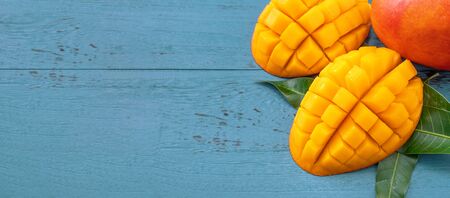 Fresh mango - Juicy chopped fruit with green leaves on  blue timber background. Tropical fruit design concept. Flat lay. Top view. Copy spaceの写真素材