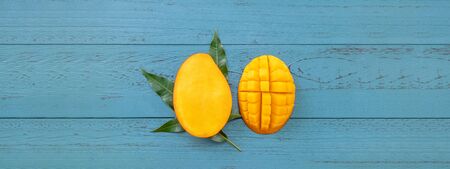 Fresh mango - beautiful chopped fruit with green leaves on dark blue timber background. Tropical...