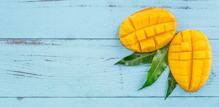 Fresh mango - beautiful chopped fruit with green leaves on bright blue timber background. Tropical fruit design concept. Flat lay. Top view. Copy spaceの写真素材