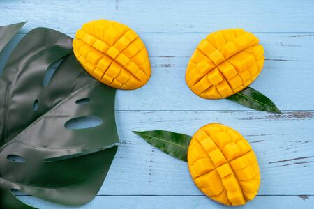 Fresh mango - beautiful chopped fruit with green leaves on bright blue timber background. Tropical fruit design concept. Flat lay. Top view. Copy spaceの写真素材