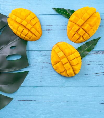 Fresh chopped mango with green leaves on bright blue timber background. Tropical fruit design concept. Flat lay. Top view. Copy spaceの写真素材