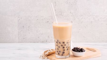 Tapioca pearl ball bubble milk tea, popular Taiwan drink, in drinking glass with straw on marble white table and wooden tray, close up, copy space.の写真素材