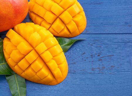 Fresh chopped mango with green leaves on dark blue timber background. Tropical fruit design concept. Flat lay. Top view. Copy spaceの写真素材