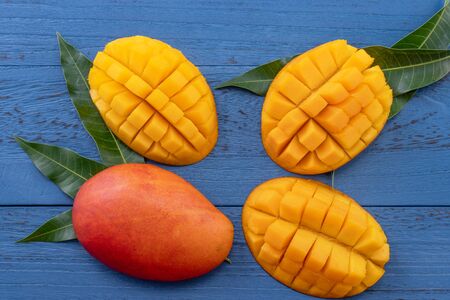Fresh chopped mango  with green leaves on dark blue timber background. Tropical fruit design concept. Flat lay. Top view.の写真素材