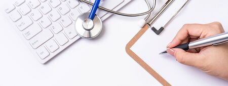Female doctor writing a medical record case over clipboard on white working table with stethoscope,...