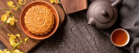 Mid-Autumn Festival traditional food concept - Beautiful Moon cake on black slate table with tea, pastry mold, flower, top view, flat lay, copy spaceの写真素材