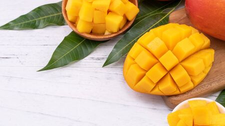Fresh chopped mango on a tray and bright rustic wooden background. Tropical summer fruit design concept, close up, macro, copy space.の写真素材