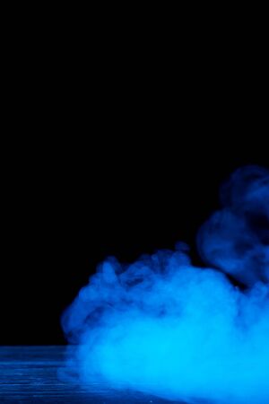 Conceptual image of blue smoke isolated on black background and wooden table.の写真素材