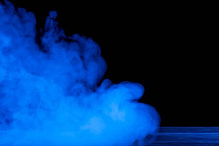 Conceptual image of blue smoke isolated on black background and wooden table.の写真素材
