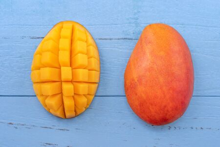 Fresh mango - beautiful chopped fruit with green leaves on bright blue timber background. Tropical fruit design concept. Flat lay. Top view. Copy spaceの写真素材