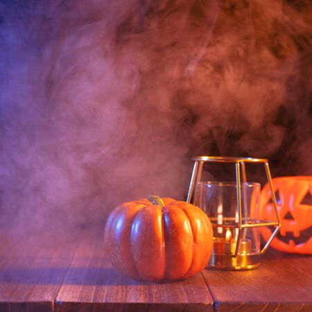 Halloween concept, orange pumpkin lantern and candles on a dark wooden table with blue-orange smoke around the background, trick or treat, close upの写真素材