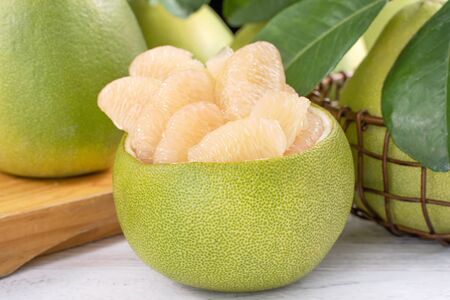 Freshly peeled pomelo, grapefruit with green leaves on bright wooden plank table. Mid-Autumn...