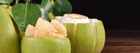 Fresh peeled pomelo, grapefruit, shaddock with green leaves on dark wooden plank table. Seasonal...