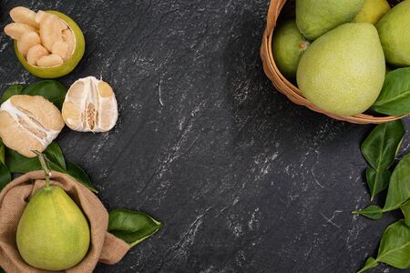 Fresh pomelo, grapefruit in bamboo basket with green leaf on dark black slate background. Seasonal fruit for Mid-Autumn Festival. Top view. Flat lay.の写真素材