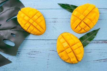 Fresh mango, beautiful chopped fruit with green leaves on dark wooden table background. Tropical fruit design concept. Flat lay. Top view. Copy spaceの写真素材