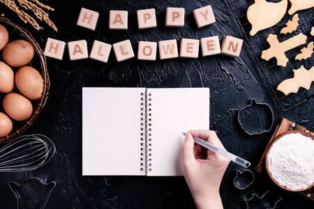 Young woman is reading and writing recipe of making Halloween cookies, design concept of preparing for Halloween party, top view, flat lay, overhead.の写真素材