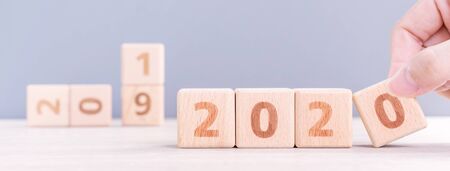 Abstract 2020 & 2019 New year countdown design concept - woman holding wood blocks cubes on wooden table and blue background, close up, copy space.の写真素材