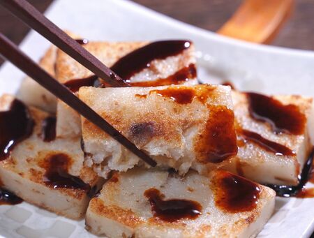 Pouring black soy sauce on ready-to-eat delicious turnip cake, Chinese traditional local dish radish cake in restaurant, close up, copy space.の写真素材