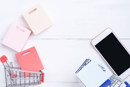 Abstract online shopping, mobile payment concept design element, colorful cart and paper bags on white wooden table background, top view, flat layの写真素材