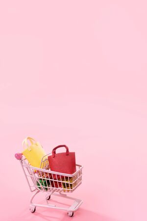 Annual sale shopping season concept - mini pink shop cart trolley full of paper bag gift isolated on pale pink background, blank copy space, close upの写真素材