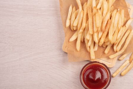 Golden yummy deep French fries on kraft baking sheet paper and serving tray to eat with ketchup and...