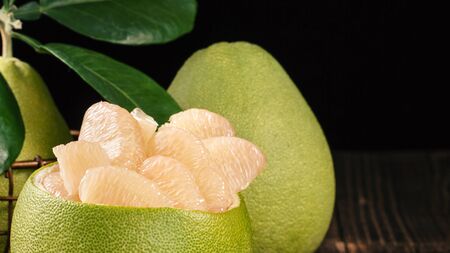 Fresh peeled pomelo, grapefruit, shaddock with green leaves on dark wooden plank table. Seasonal...