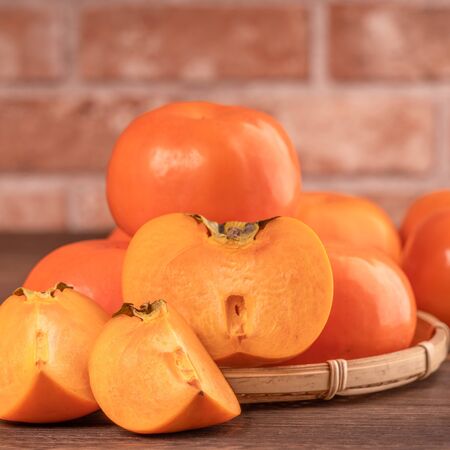 Fresh beautiful sliced sweet persimmon kaki on dark wooden table with red brick wall background, Chinese lunar new year fruit design concept, close up.の写真素材