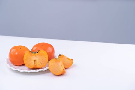 Fresh beautiful sliced sweet persimmon kaki isolated on white kitchen table with gray blue background, Chinese lunar new year design concept, close up.の写真素材