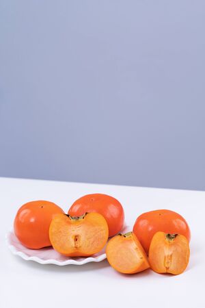 Fresh beautiful sliced sweet persimmon kaki isolated on white kitchen table with gray blue background, Chinese lunar new year design concept, close up.の写真素材