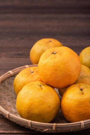 Fresh, beautiful orange color tangerine on bamboo sieve over dark wooden table. Seasonal, traditional fruit of Chinese lunar new year, close up.の写真素材