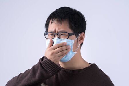 Young Asian man is coughing, feeling unwell, vomit sick with wearing a medical blue face mask...