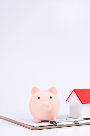 Financial concpet - Piggy bank, beautiful red white wooden house model on white background, saving money to buy insurance, close up, copy space.の写真素材