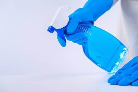 Young woman housekeeper is doing cleaning white table in apron with blue gloves, spray cleaner, wet yellow rag, close up, copy space, blank design concept.の写真素材