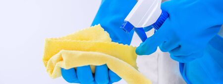 Young woman housekeeper is doing cleaning white table in apron with blue gloves, spray cleaner, wet...