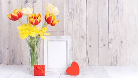 Tulip flower in glass vase with picture frame decor on wooden table background wall at home, close...
