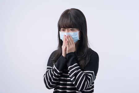 Woman coughing with mask - young Asian covering the mouth, feeling unwell with wearing medical blue face mask isolated on white background, close up.の写真素材