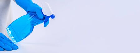 Young woman housekeeper is doing cleaning white table in apron with blue gloves, spray cleaner, wet...