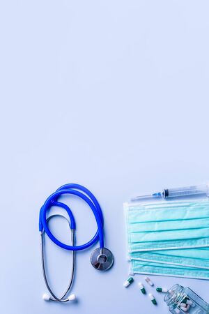 Mask with pills, stethoscope, syringe medical supply objects isolated on blue background, top view, flat lay, overhead shot, virus protection concept.の写真素材