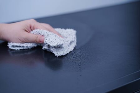 Young woman is holding spray bottle, rag to clean, wipe down office metal cabinet shelf...