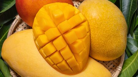 Mango, tropical fruit, in a bamboo wooden sieve basket on green leaf background, top view, full frame, beautiful, ripe harvest design concept.の写真素材