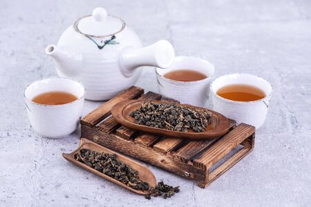 Hot tea in white teapot and cups on a sieve over bright gray cement background, closeup, copy space design concept.の写真素材